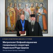 Митрополит Епіфаній і пастор із орденом на блакитній стрічці та футляром у руках на тлі образу святих Київської землі; напис «Орден Архистратига Михаїла II ступеня»