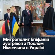 Митрополит Епіфаній у чорному клобуку вітає Посла Німеччини Бориса Руґе та співробітників Посольства; на столі прапорці Німеччини й України, позаду картина зі святими; напис «Митрополит Епіфаній зустрівся з Послом Німеччини в Україні»