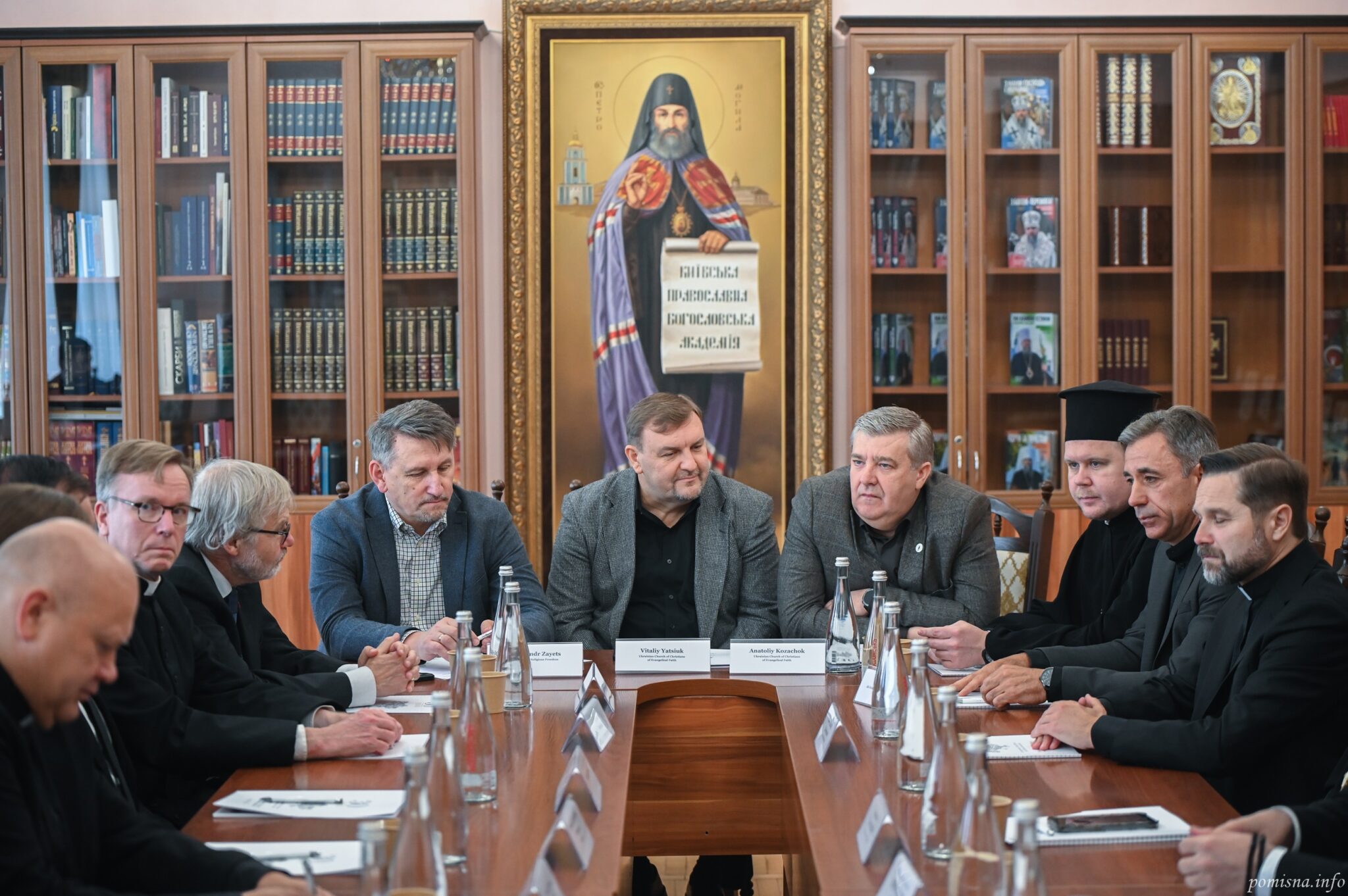 Учасники зустрічі за столом на тлі образу святителя Петра Могили з сувоєм «Київська православна богословська академія»